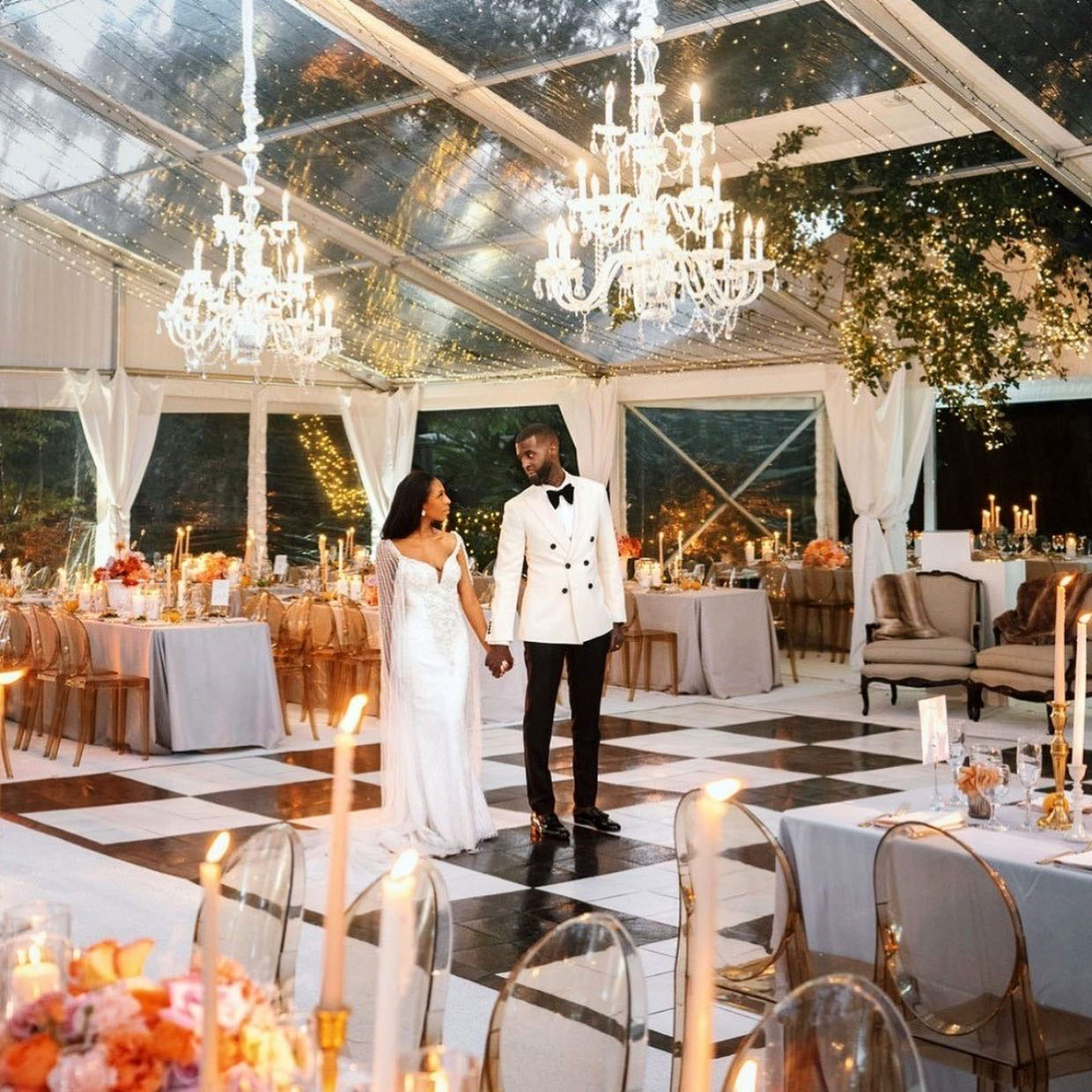 Couple standing on slate black and slate white dance floor in tent wedding space with chandeliers