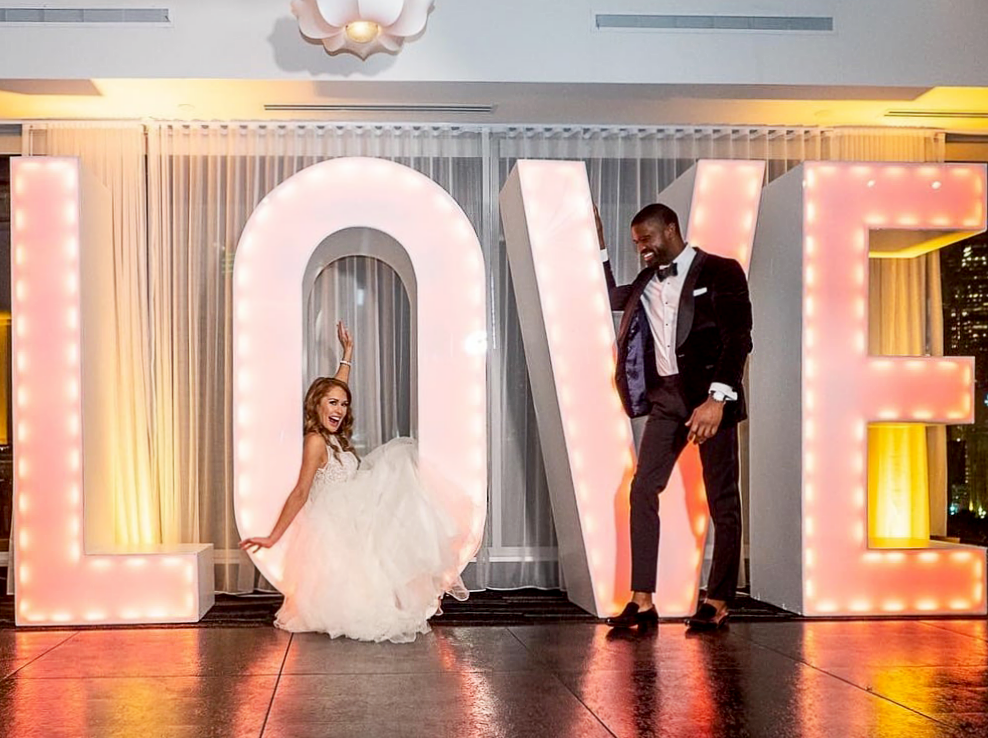Bride and Groom posing in front of LOVE sign on a Slate Black Plus style dance floor