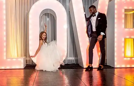A slate black dance floor with a bride, groom, and a giant sign that says love.